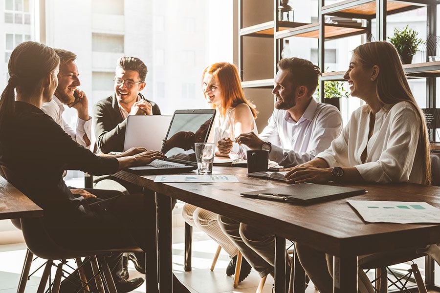 Employee Benefits - Group of Happy Employees Sitting Around Table in Office During Meeting