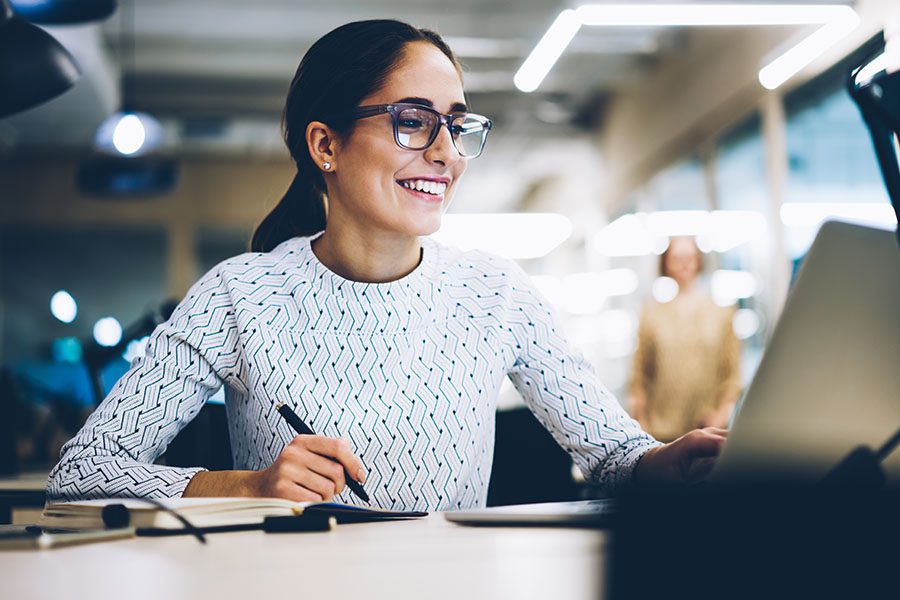 Plan Administration and Compliance - Business Woman Sitting at Desk in the Office Working on a Laptop